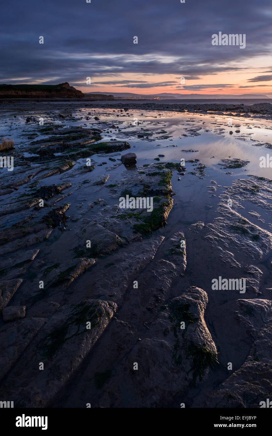 Wet limestone rocks reflect the glow of a sunset at Kilve Beach, Somerset. Stock Photo