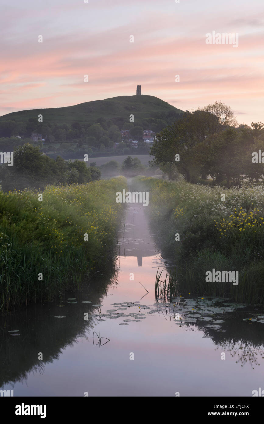 Mist shrouds Glastonbury Tor during a colourful spring sunrise on the Somerset Levels Stock