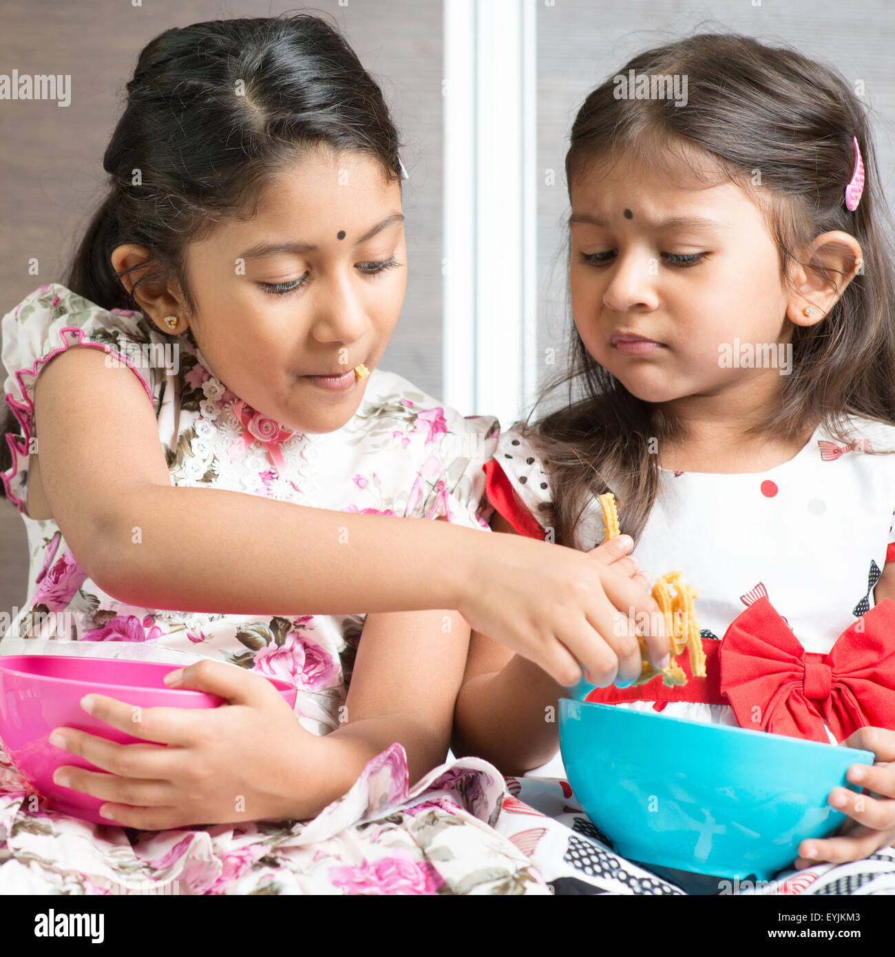 Indian girls sharing food, traditional snack murukku with each other. Asian sibling or children living lifestyle at home. Stock Photo