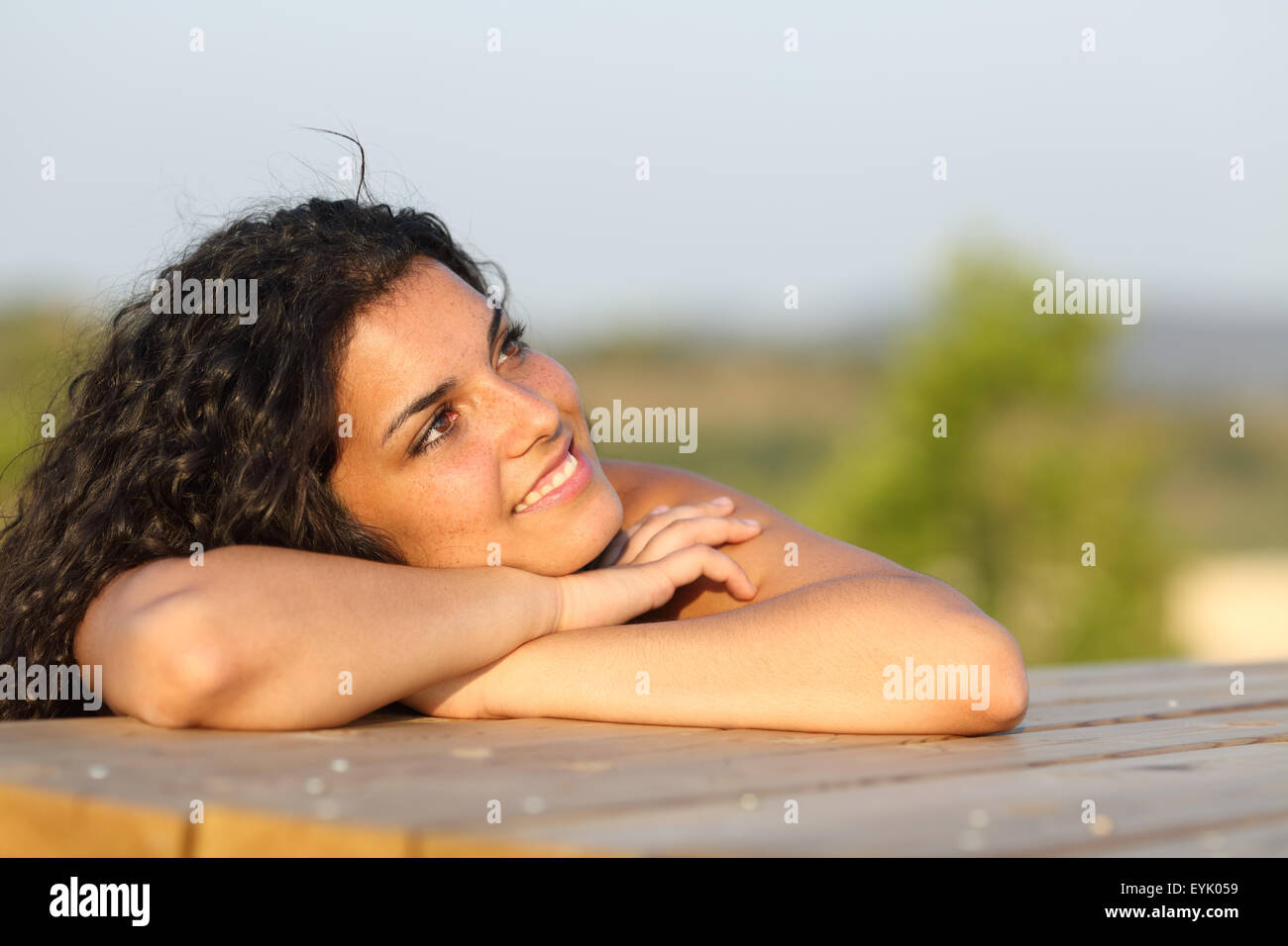 Candid girl thinking and looking sideways relaxing in a park at sunset with the sky in the background Stock Photo