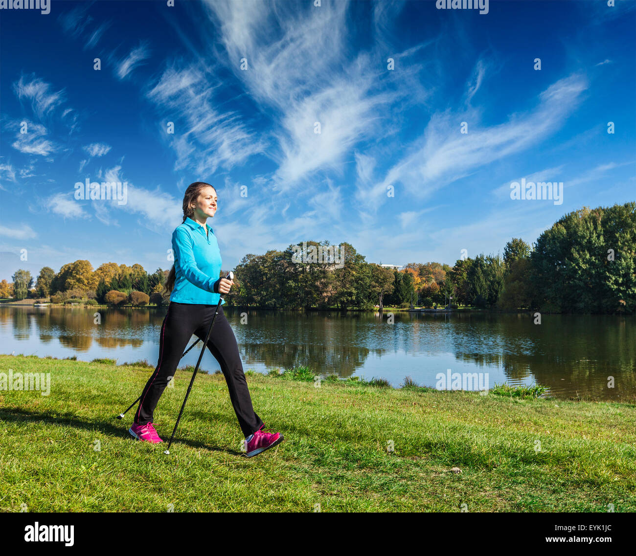 Nordic walking adventure and exercising - young woman hiking with nordic walking poles in park along river Stock Photo