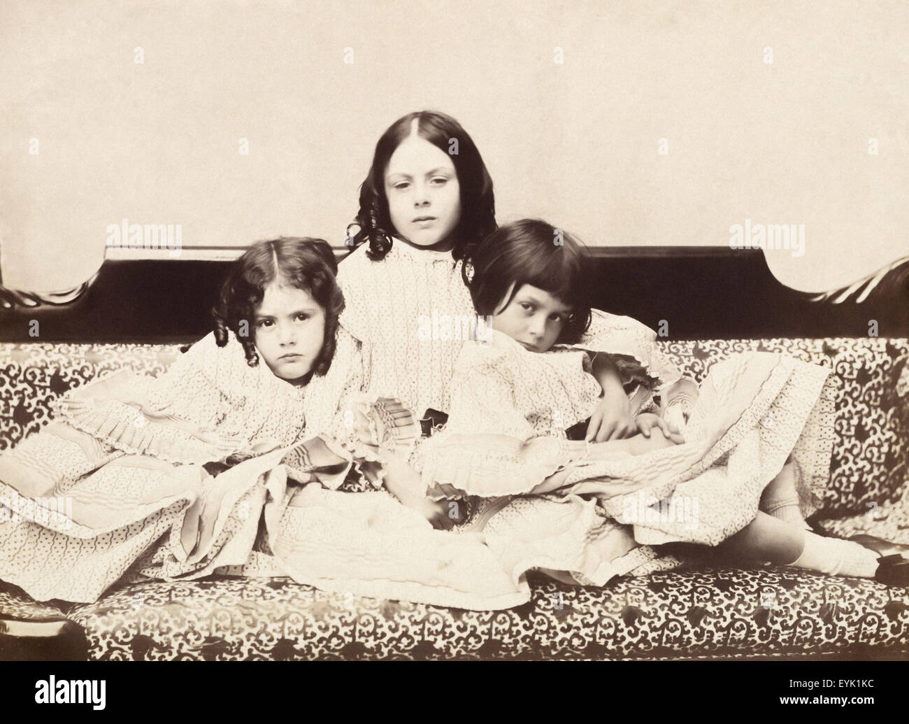 Alice Liddell (1852-1934) (right) with her sisters Edith (left) and Lorina (center) on a chaises longue. Alice Liddell is the namesake and inspiration behind Alice in Wonderland. Photographed by Charles Lutwidge Dodgson (1832-1898) better known as Lewis Carroll in 1858. Lewis Carroll made up some tales of Alice and her adventures down the rabbit hole to entertain them on a boating trip down the Isis in Oxfordshire in 1862. Stock Photo
