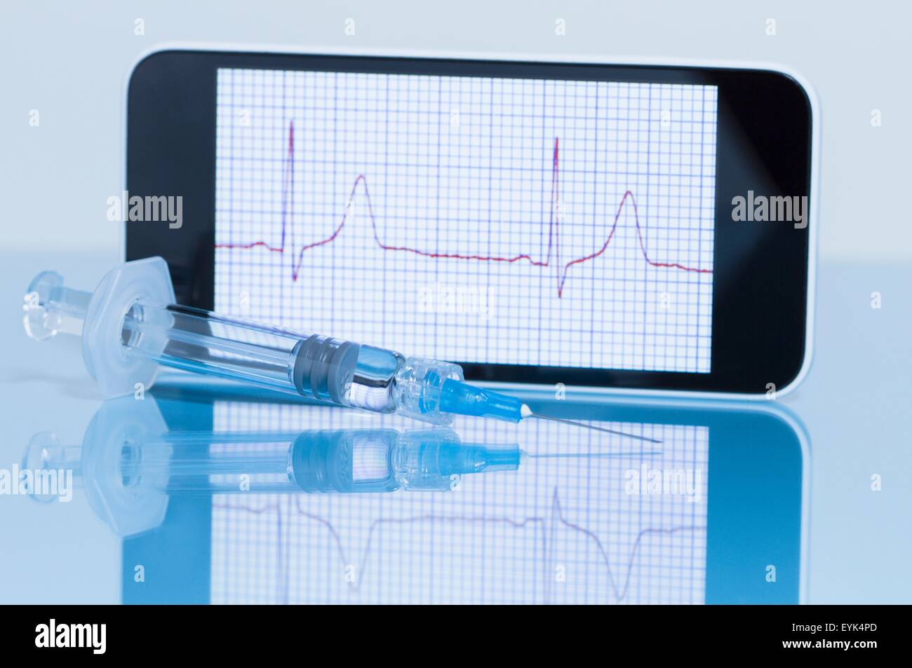 Smart phone displaying an electrocardiogram, disposable syringe in foreground Stock Photo
