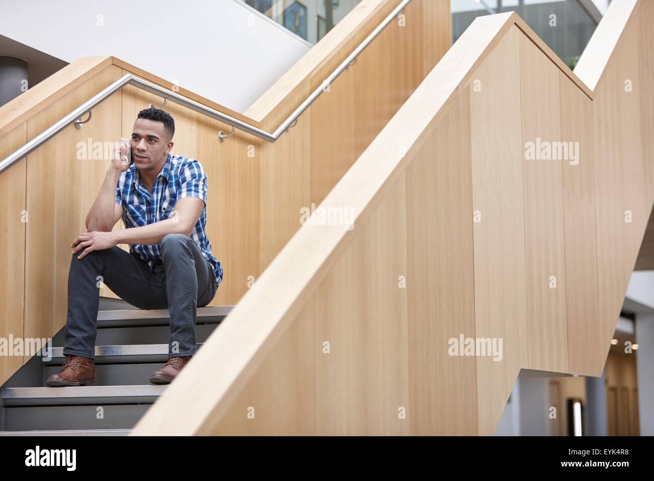 Young businessman sitting on office stairway chatting on smartphone Stock Photo