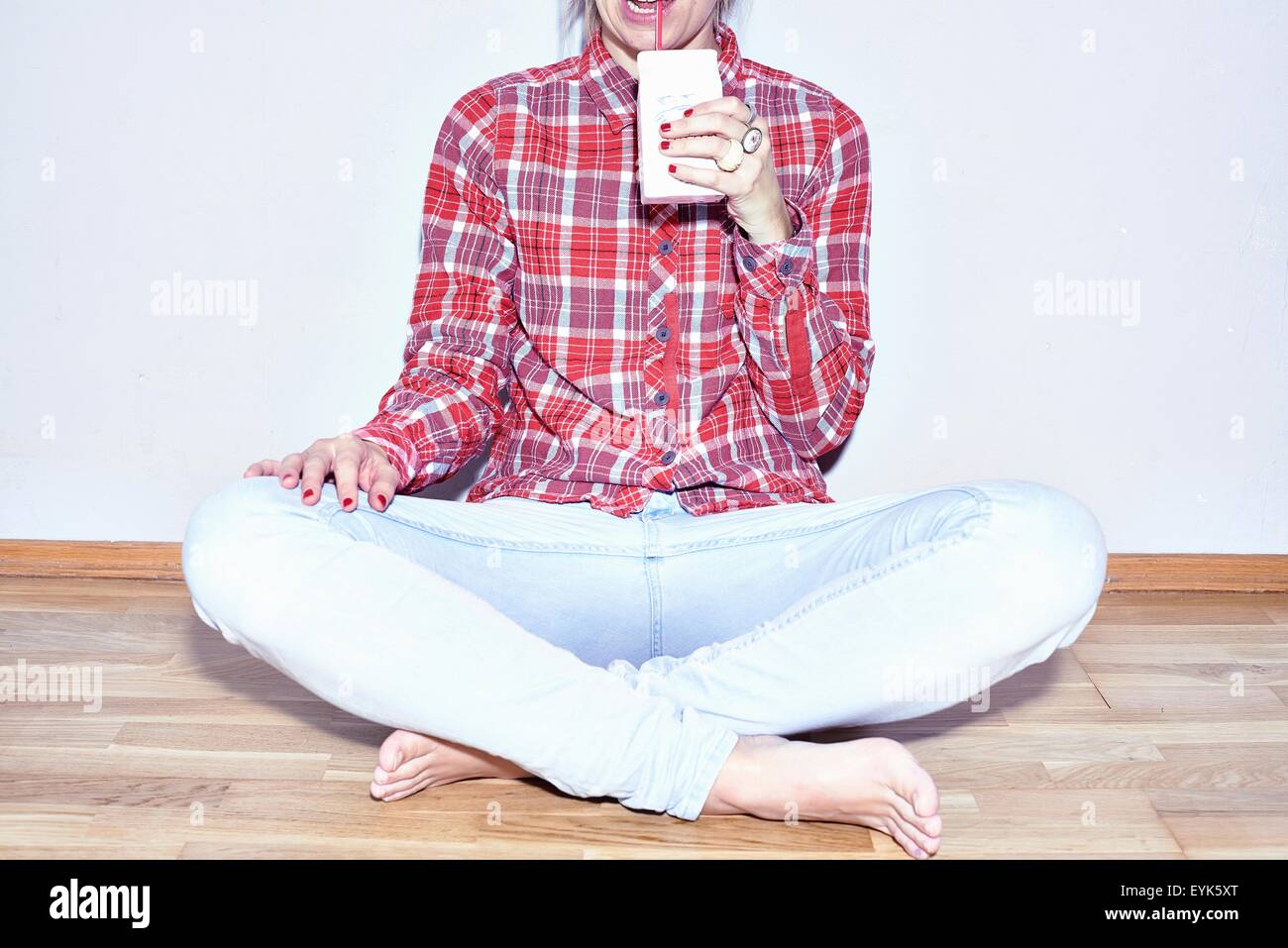 Studio shot of young woman sitting on floor drinking juice Stock Photo