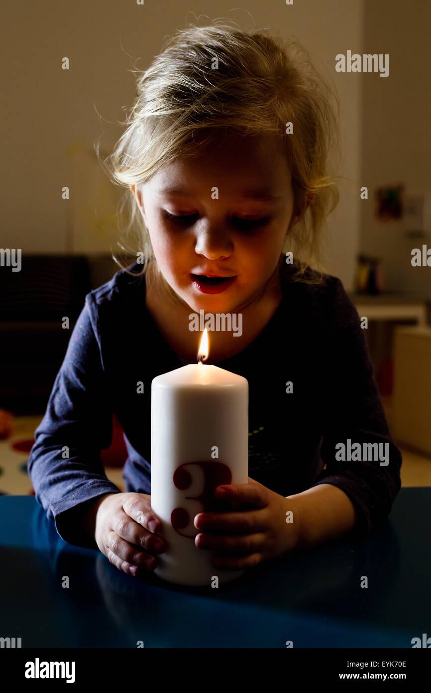 Girl holding lit candle in dark Stock Photo