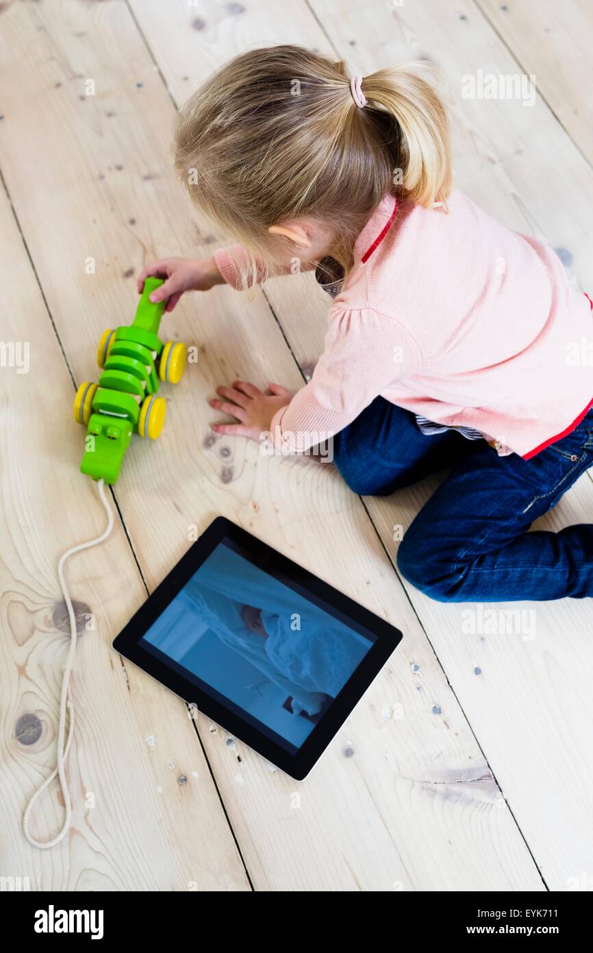Girl with digital tablet, playing toy on wooden floor Stock Photo