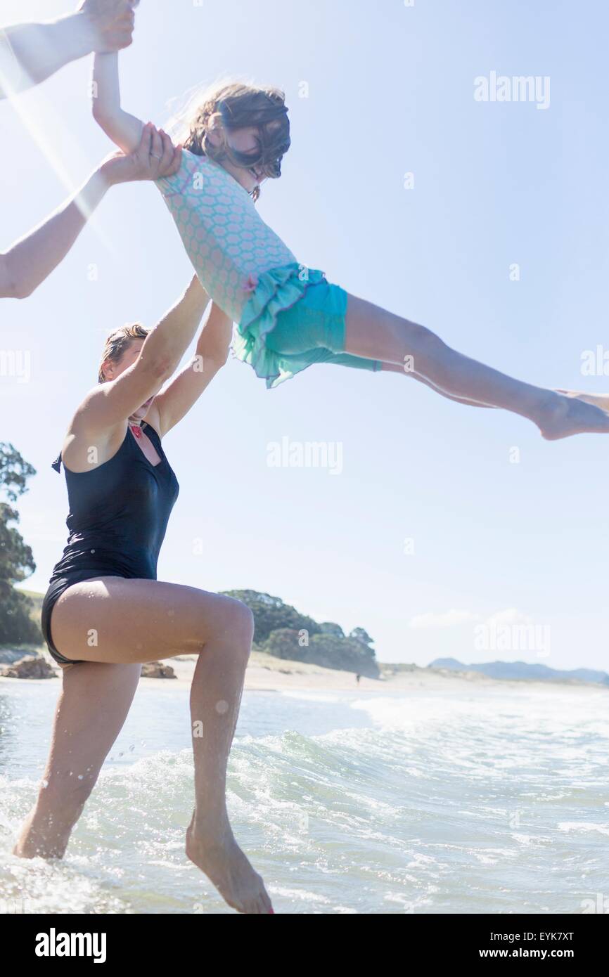 Two women lifting girl over ocean waves, Hot Water Beach, Bay of Islands, New Zealand Stock Photo