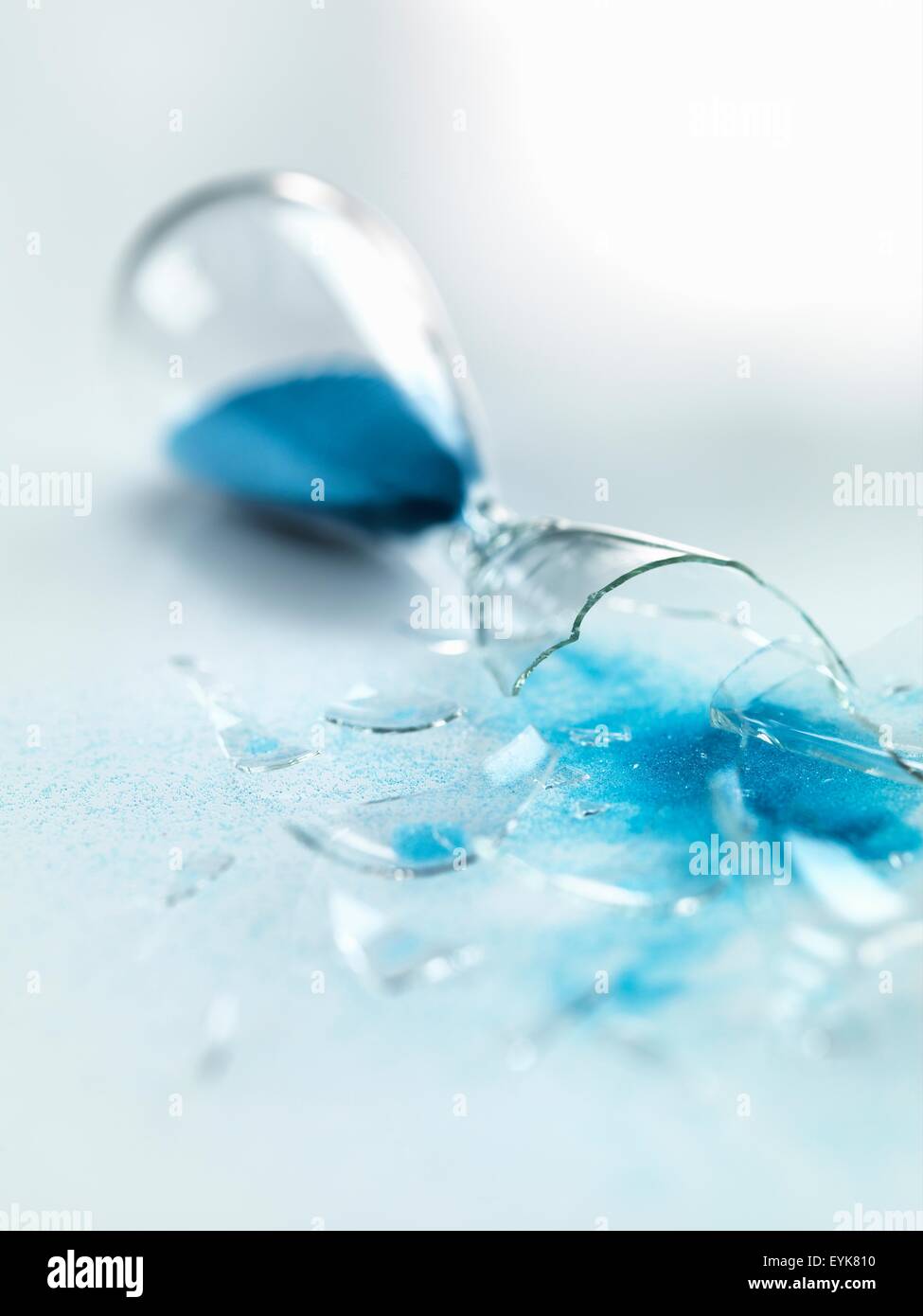 Blue sand pouring out of broken glass hourglass Stock Photo