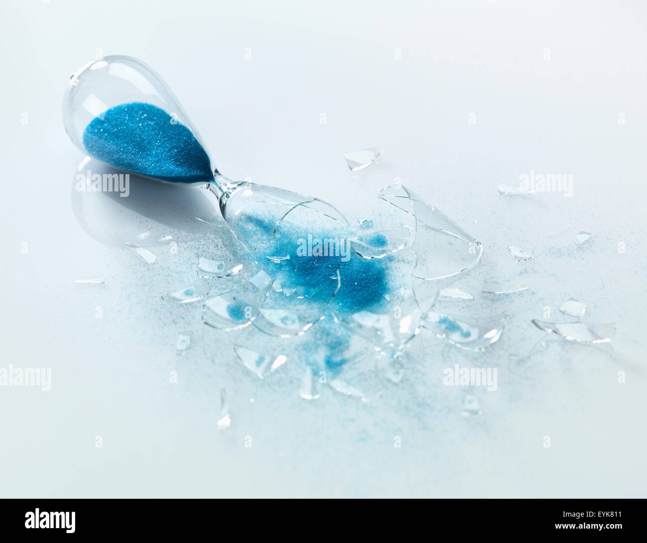 Broken glass hourglass with blue sand pouring out Stock Photo