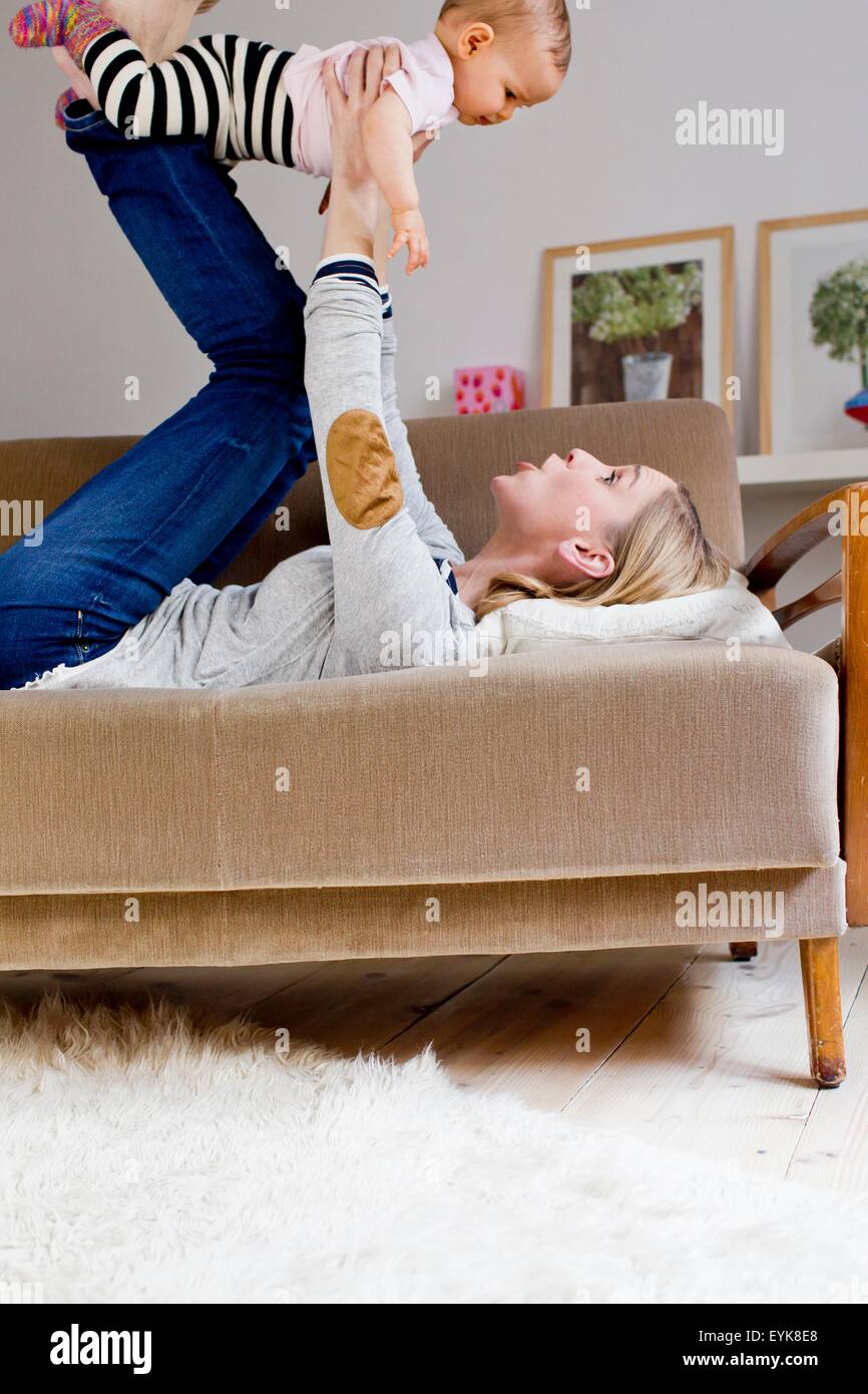 Mother lying on sofa, holding baby girl in air Stock Photo