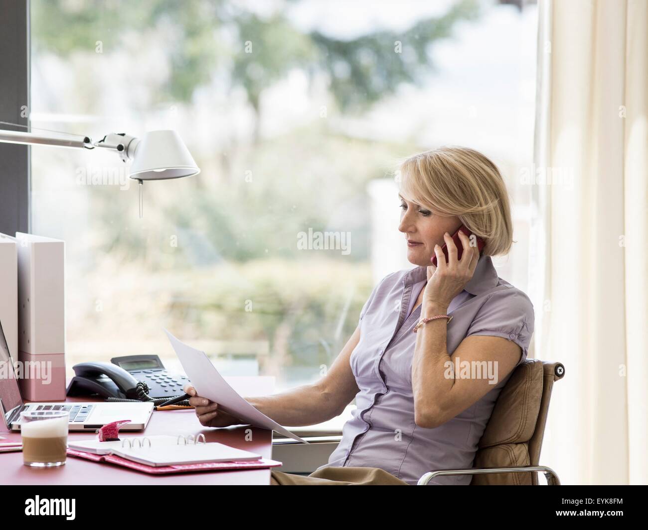 Mature businesswoman talking on smartphone at home desk Stock Photo