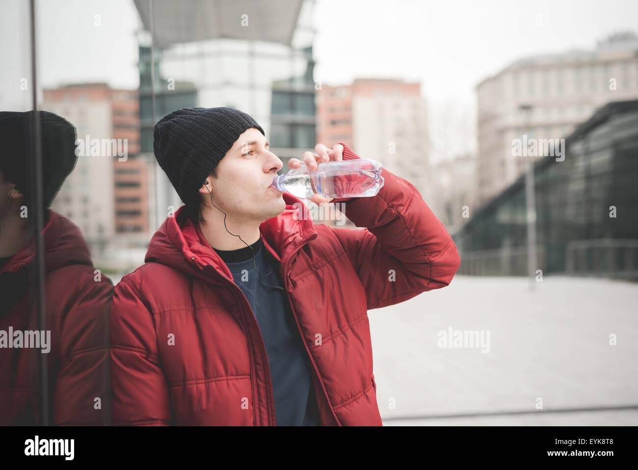 Young man leaning against office building drinking water Stock Photo