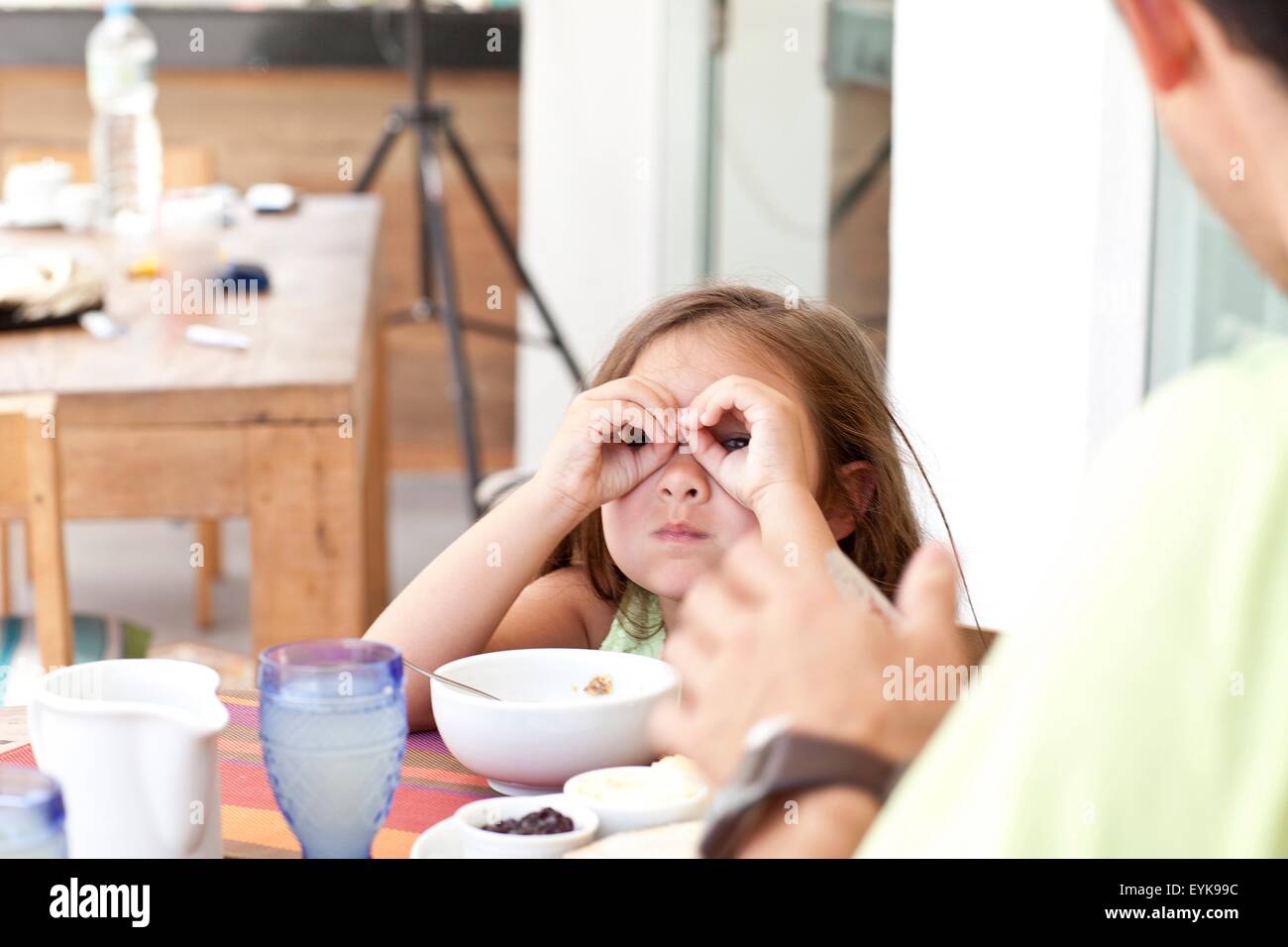 Father and daughter sitting at breakfast table, daughter making binoculars from fingers Stock Photo
