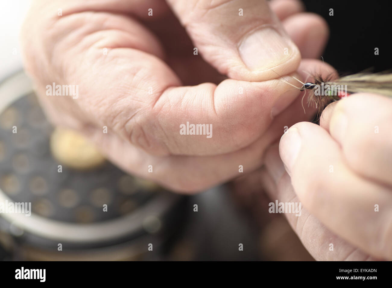 Closeup view of a man holding an imitation insect artificial fly, fishing reel in background Stock Photo