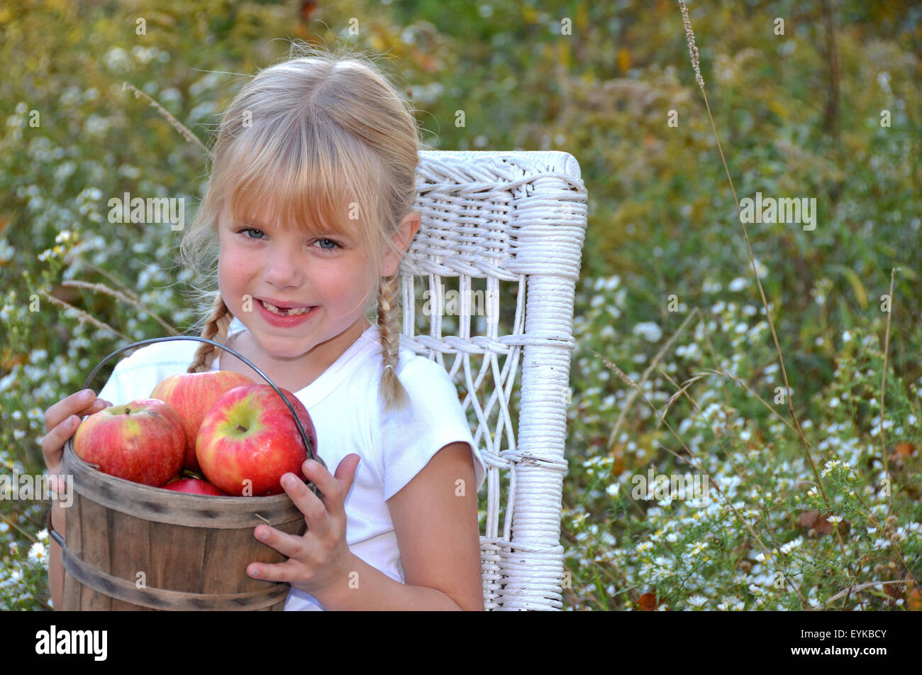 Happy little girl sitting on a white wicker chair with a bushel of ...
