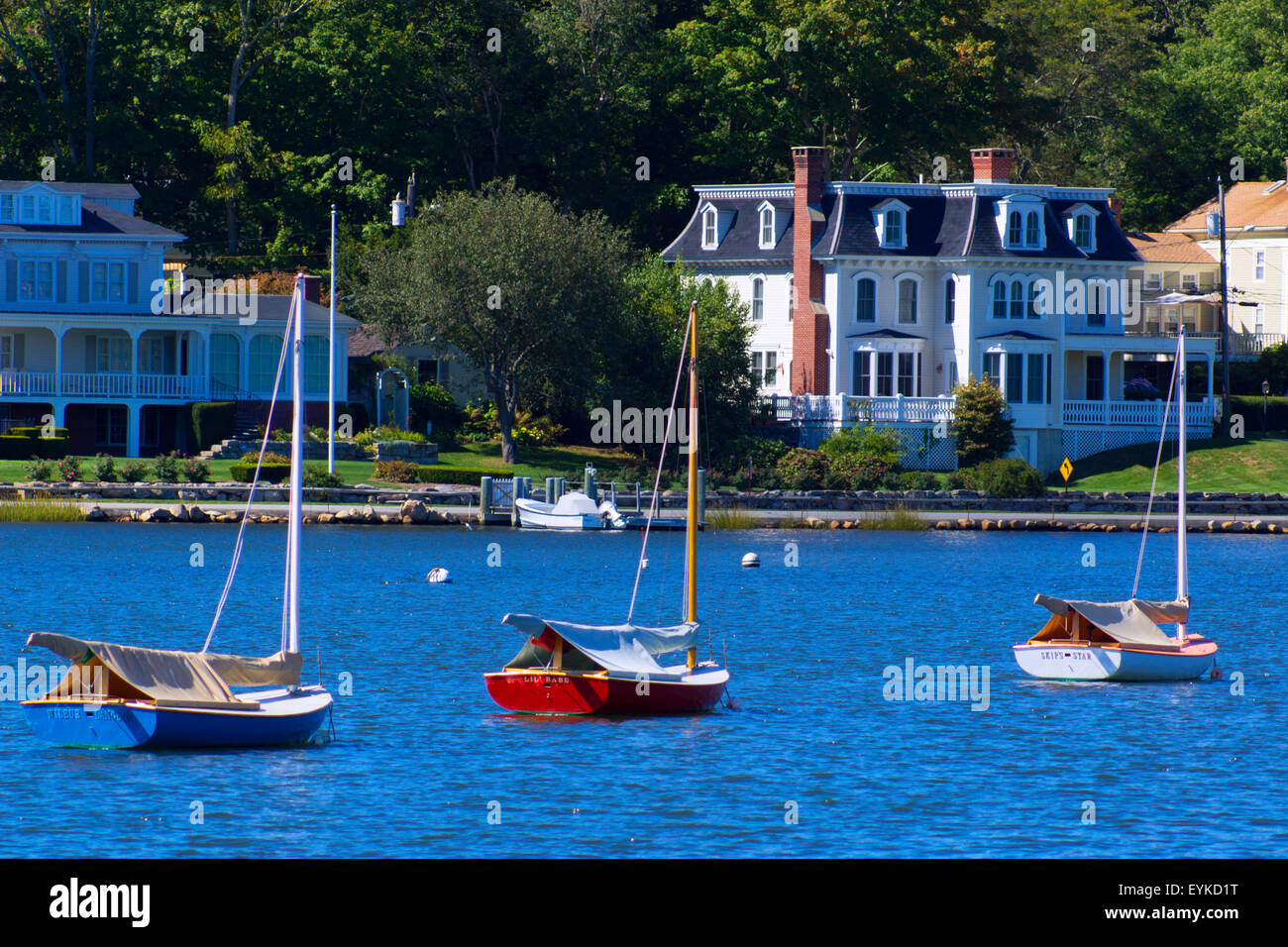 Three small sailboats are moored in front of several beautiful home in this coastal photograph. Stock Photo