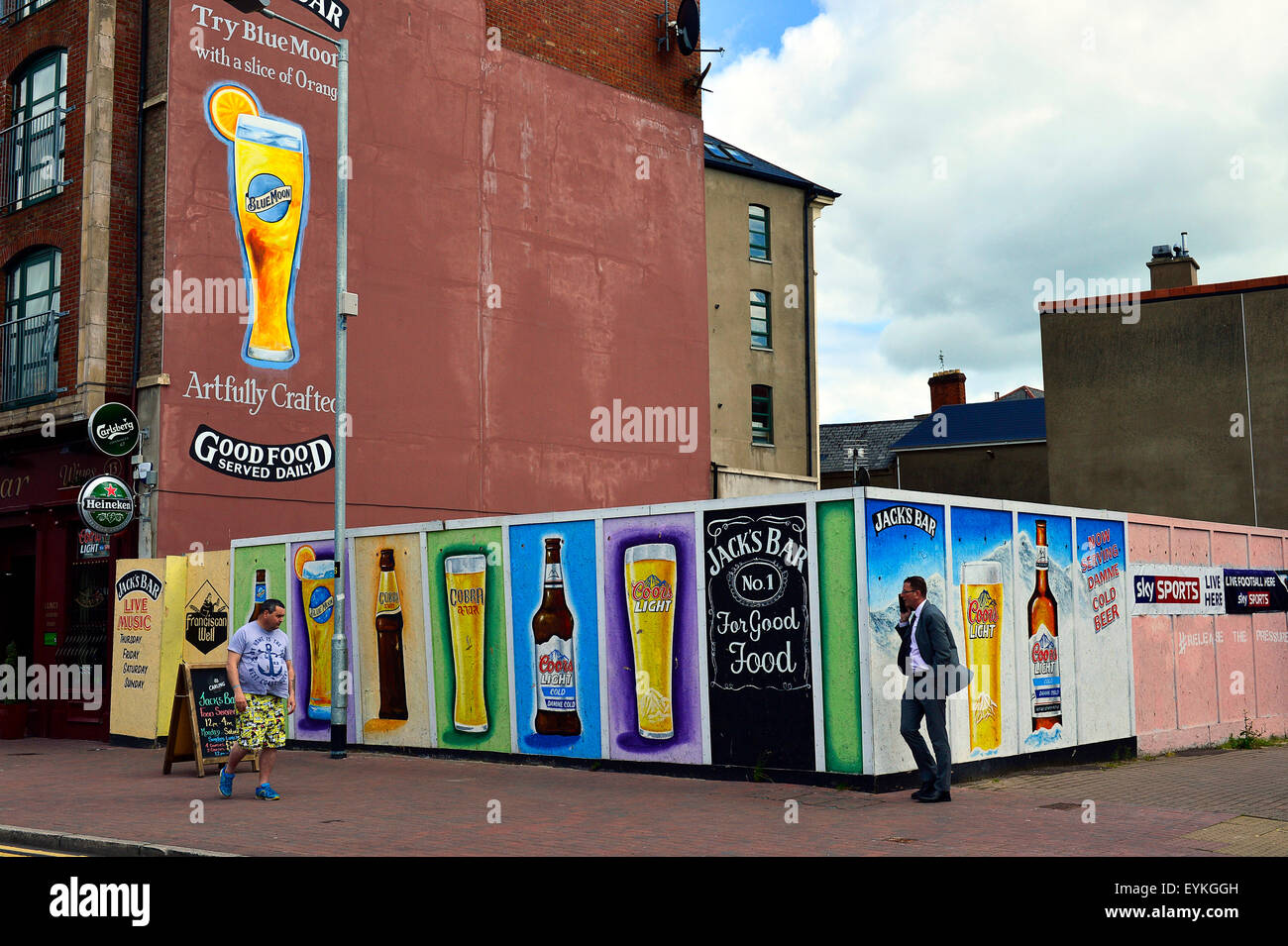 People walking past billboards advertising alcohol outside a pub in Londonderry (Derry), Northern Ireland Stock Photo