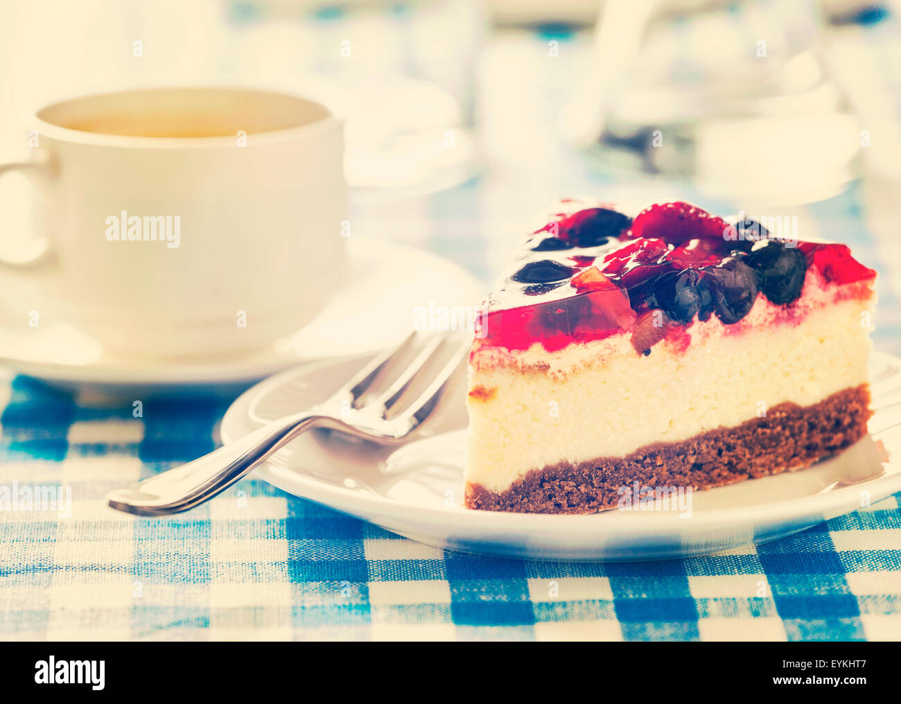 Vintage retro effect filtered hipster style image of dessert fruit cheese cake on plate with fork and coffee cup on blue checker Stock Photo