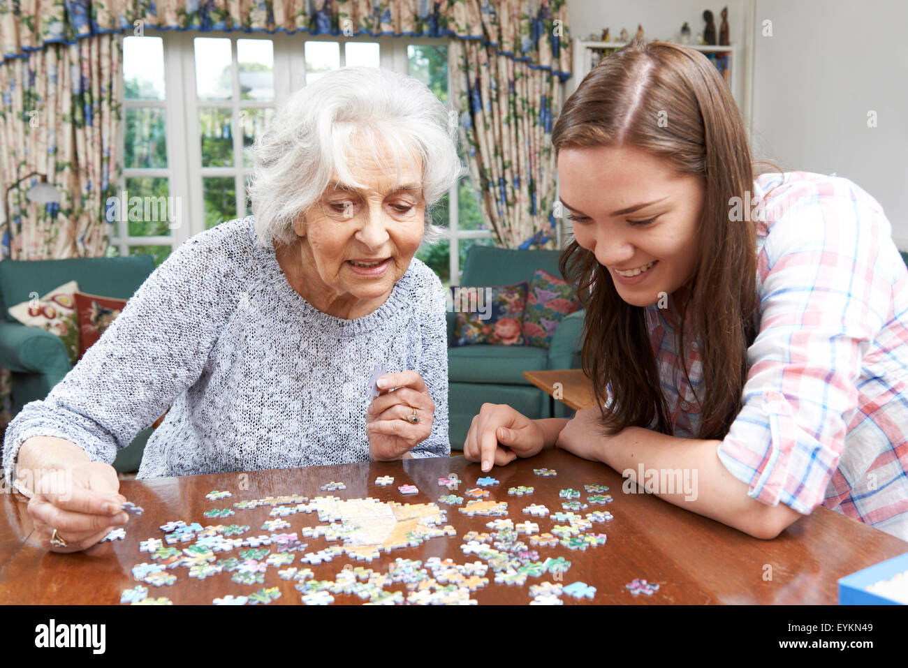 Teenage Granddaughter Helping Grandmother With Jigsaw Puzzle Stock Photo