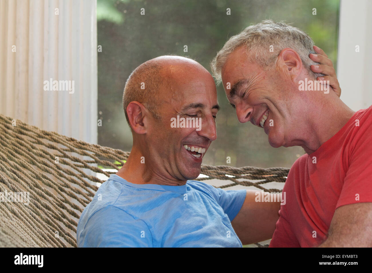 Senior gay male couple on vacation being affectionate in hammock at bed and breakfast Stock Photo