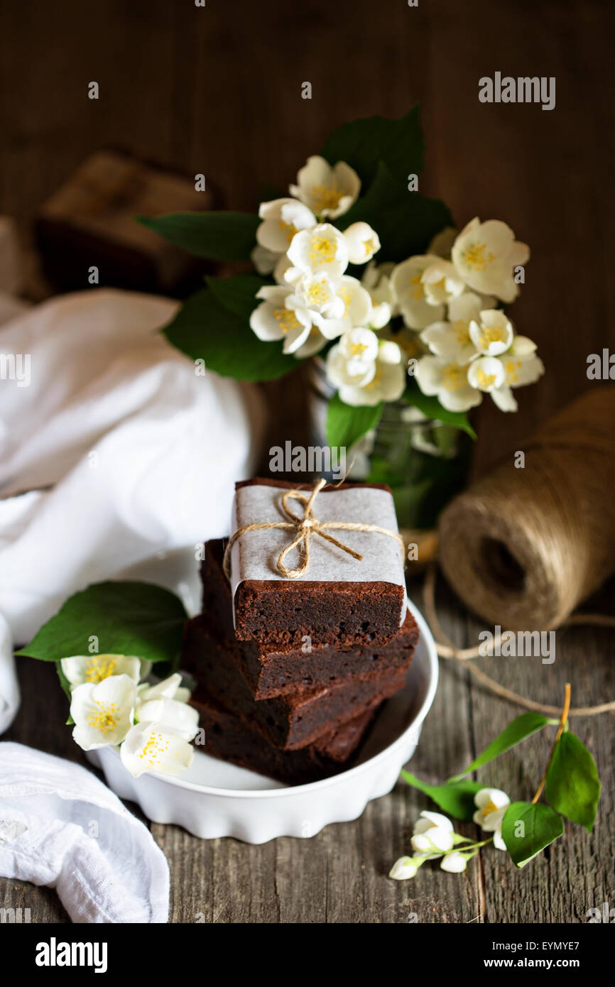 Chocolate mascarpone brownies stacked with flowers on wooden table Stock Photo