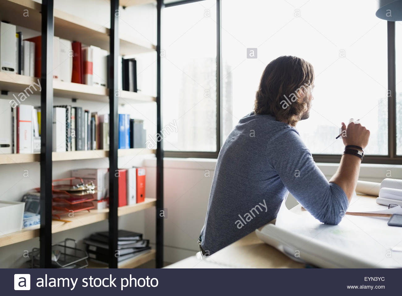 Pensive architect drafting blueprints looking out window Stock Photo