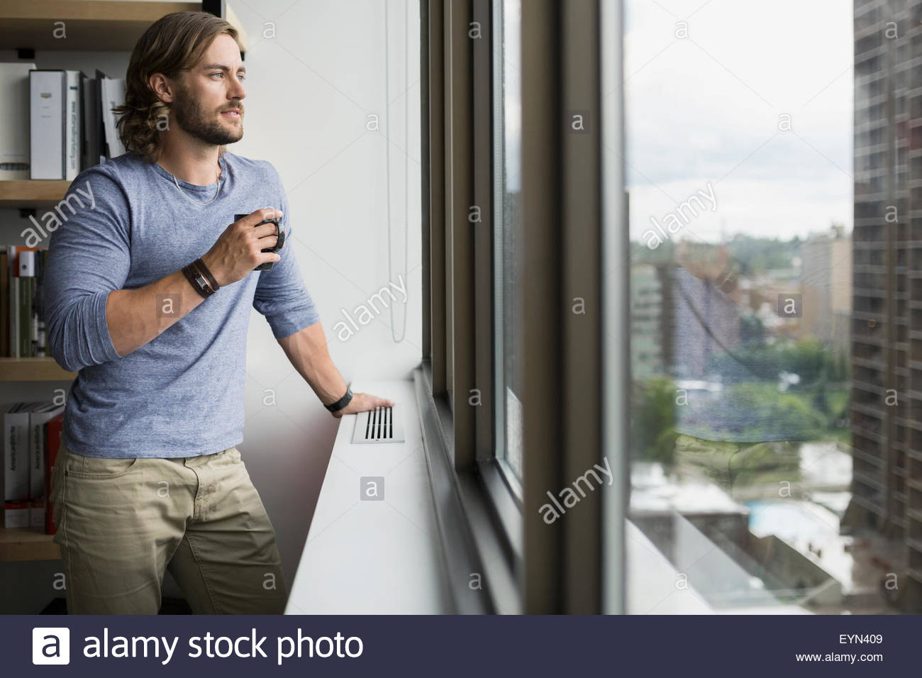 Pensive businessman drinking coffee looking out office window Stock Photo