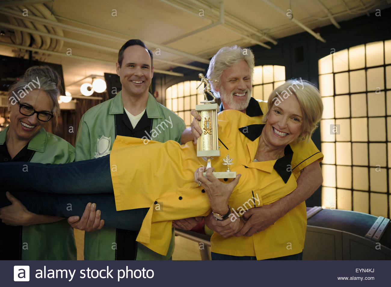Teammates holding woman with trophy in bowling alley Stock Photo