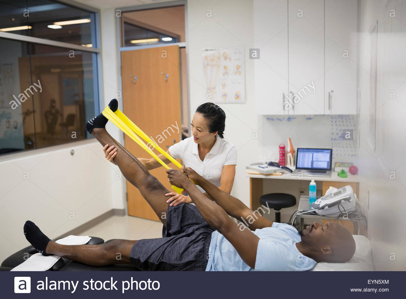 Physical therapist guiding patient using resistance band leg Stock