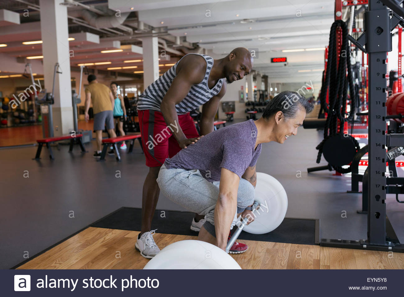 Personal trainer spotting man doing barbell deadlift gym Stock Photo