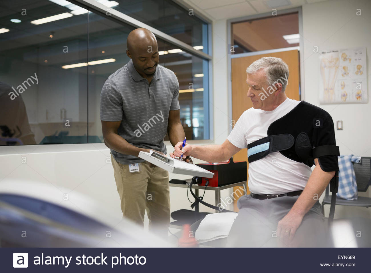 Patient in shoulder wrap signing waiver physical therapist Stock Photo