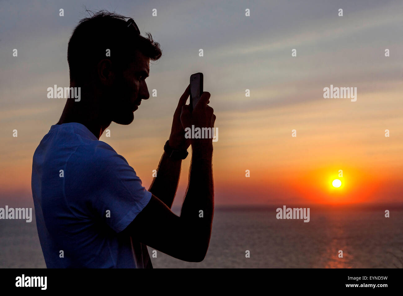 A young man taking a photo on mobile phone, Sunset Oia Santorini sunset Greece side silhouette person Stock Photo