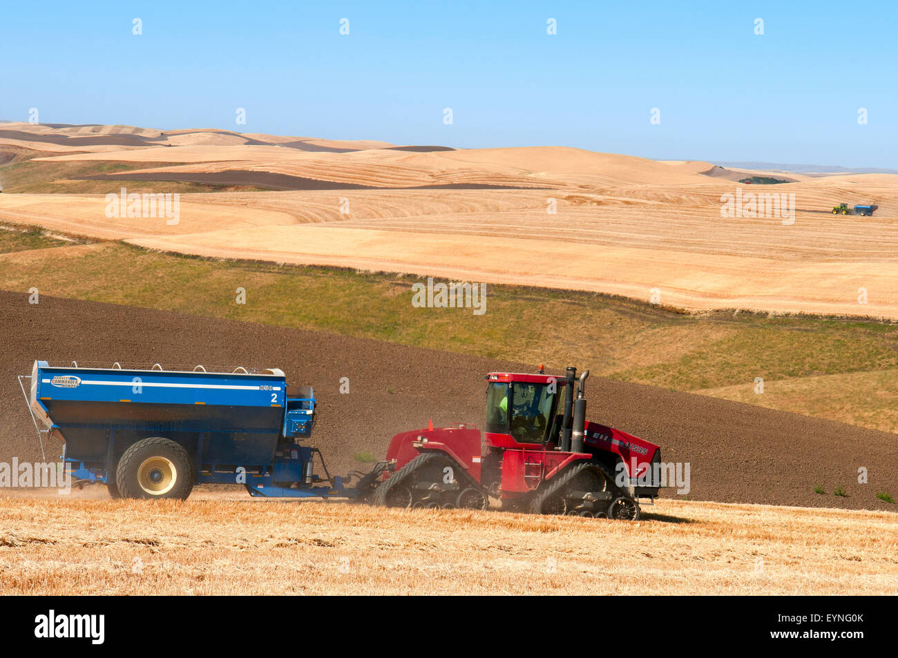 Tractor pulling a grain cart traverses a field during harvest in the Palouse region of Washington Stock Photo