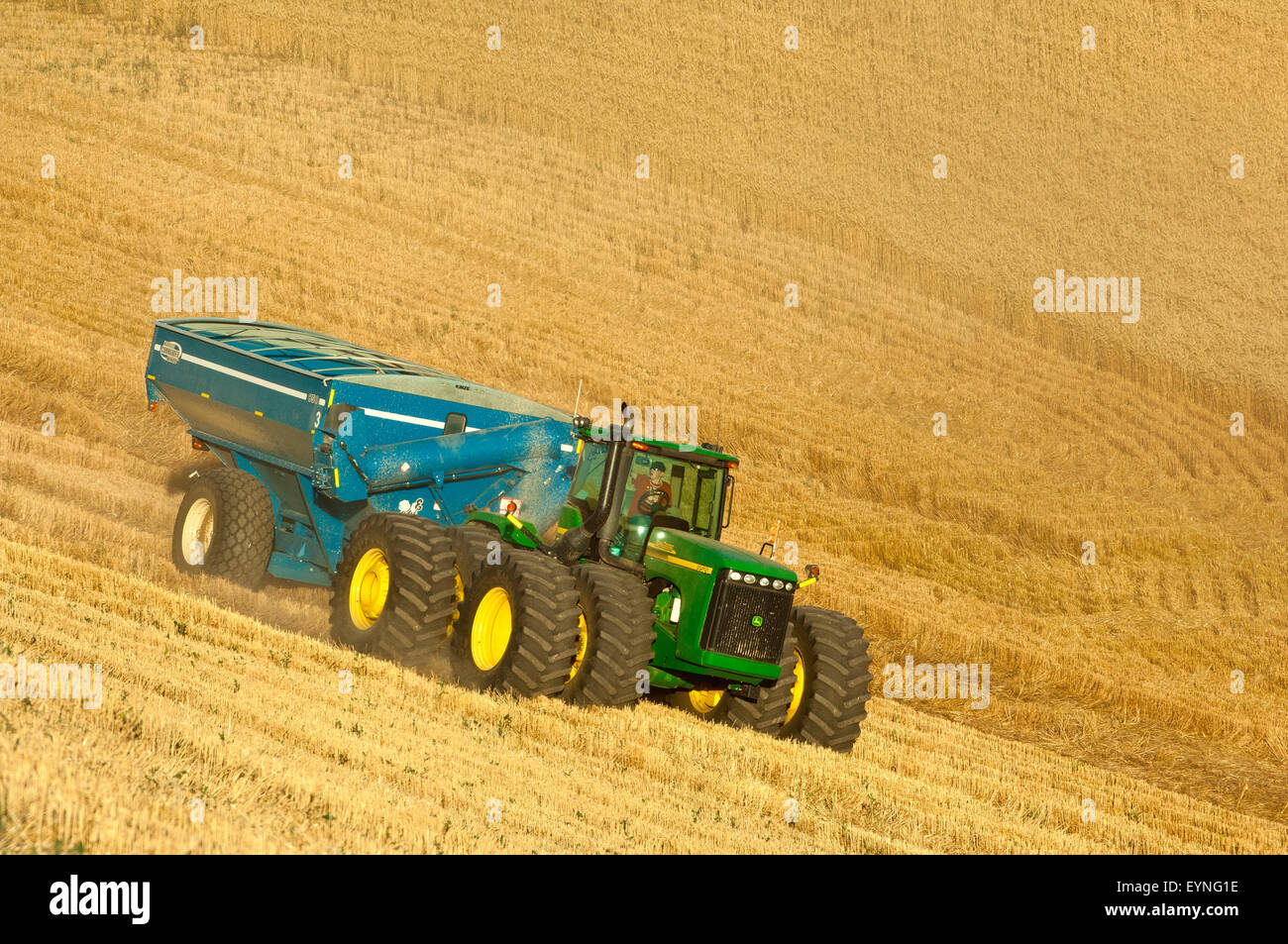 Tractor pulling a grain cart traverses a wheat field during harvest in the Palouse region of Washington Stock Photo