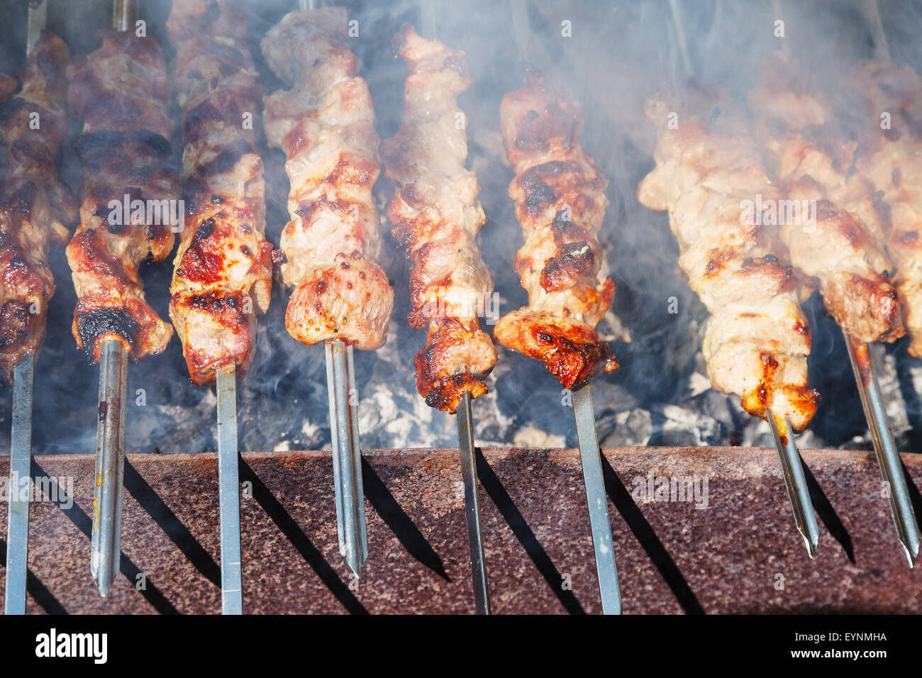 many shish kebab skewers preparing on outdoor grill Stock Photo