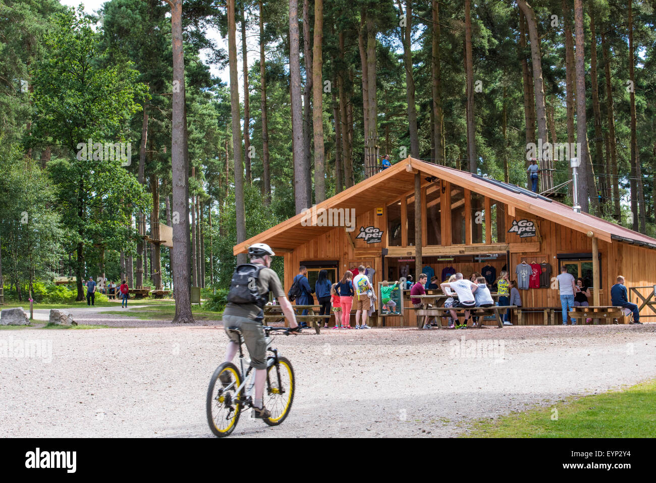 A man cycling and people sitting on benches outside Go Ape activity centre cannock chase Staffordshire West Midlands UK Stock Photo