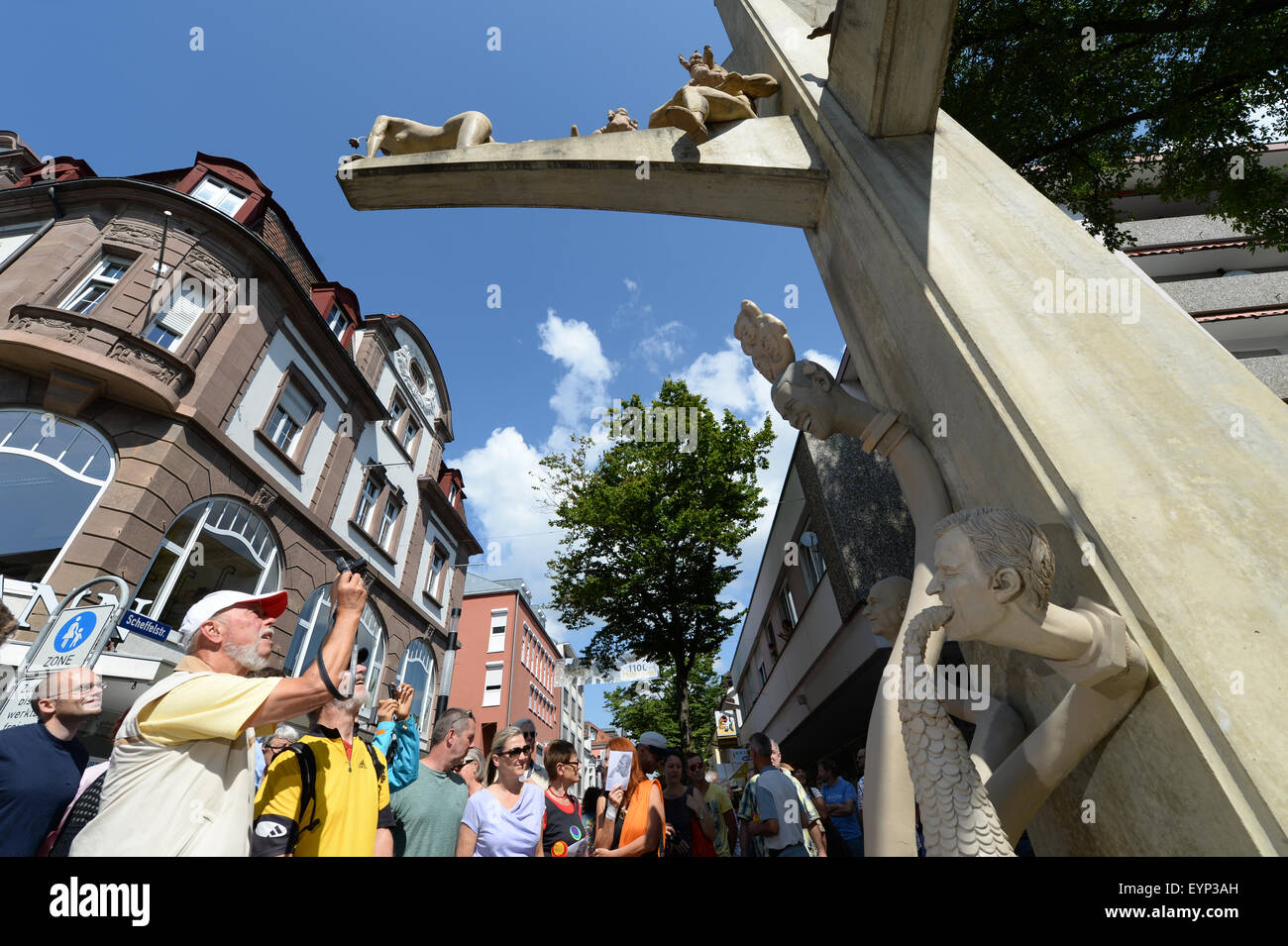 Dozens of spectators look at the newly unveiled sculpture entitled 'Paradiesschlange' (lit. paradise snake) by artist Peter Lenk in Singen am Hohentwiel, Germany, 02 August 2015. The new figures and faces will complement Lenk's existing paradise tree sculpture. The head on the bottom right depicts Dieter Schwarz, CEO of discount supermarket chain Lidl, who is 'puking money' according to Lenk. Other heads featured include US President Barack Obama, German Chancellor Angela Merkel, North Korean dictator Kim Jong-un and Russian President Vladimir Putin. Photo: FELIX KAESTLE/dpa Stock Photo