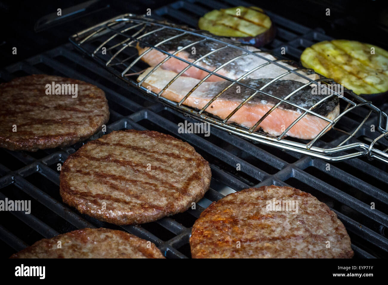 Hamburger slices, salmon steak and eggplant on grill rack, soft focus Stock Photo