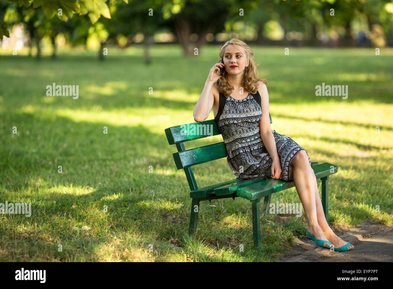 Young beautiful woman sitting on a Park bench talking on a cell phone ...