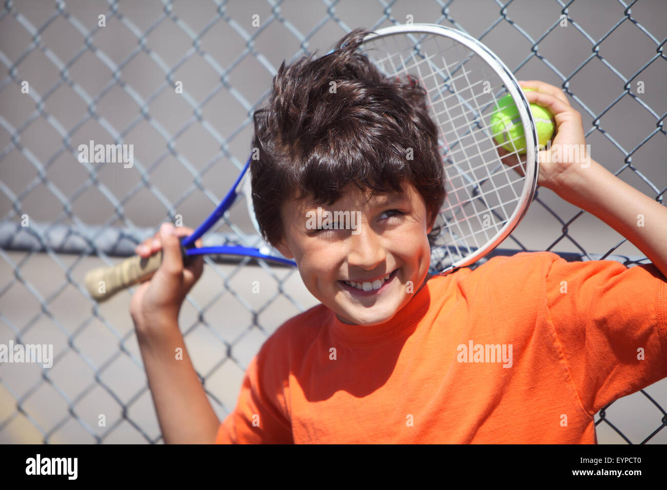 Young happy smiling boy outside in sun with tennis racket and ball Stock Photo