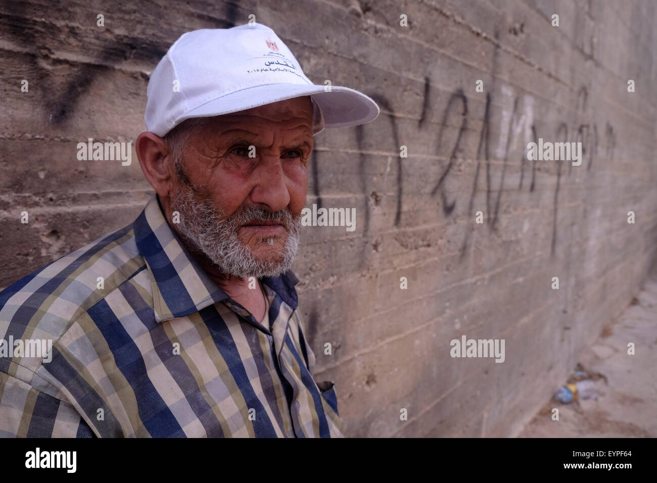 An elderly Palestinian stands next to a Hebrew phrase ‘Long live the king messiah’ spray-painted on the wall in front of Dawabsha family in Duma, a Palestinian Arab town in the West Bank which was firebombed on 31 of July by masked attackers in apparent price tag attack killing 18-month-old Ali Saad Dawabsha and critically injuring his parents and 4-year-old brother  02 August 2015. “Price tag” is used to refer to acts of political violence carried out by right-wing Israelis protesting Israeli government policy regarding the settlements and the Palestinians. Stock Photo