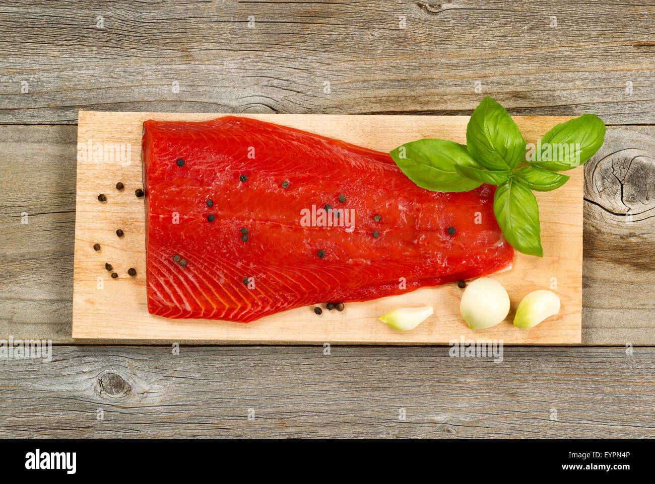 Top view shot of fresh red salmon fillet on cedar cooking board with peppercorn, garlic and basil. Aged wood underneath. Stock Photo
