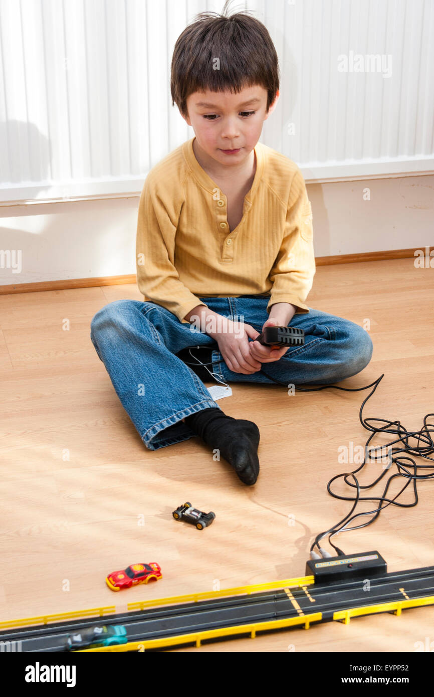 Caucasian child, boy, 6-7 year old. Indoors, sitting down on wooden floor playing with scalextric racing car set looking very absorbed and contented. Stock Photo