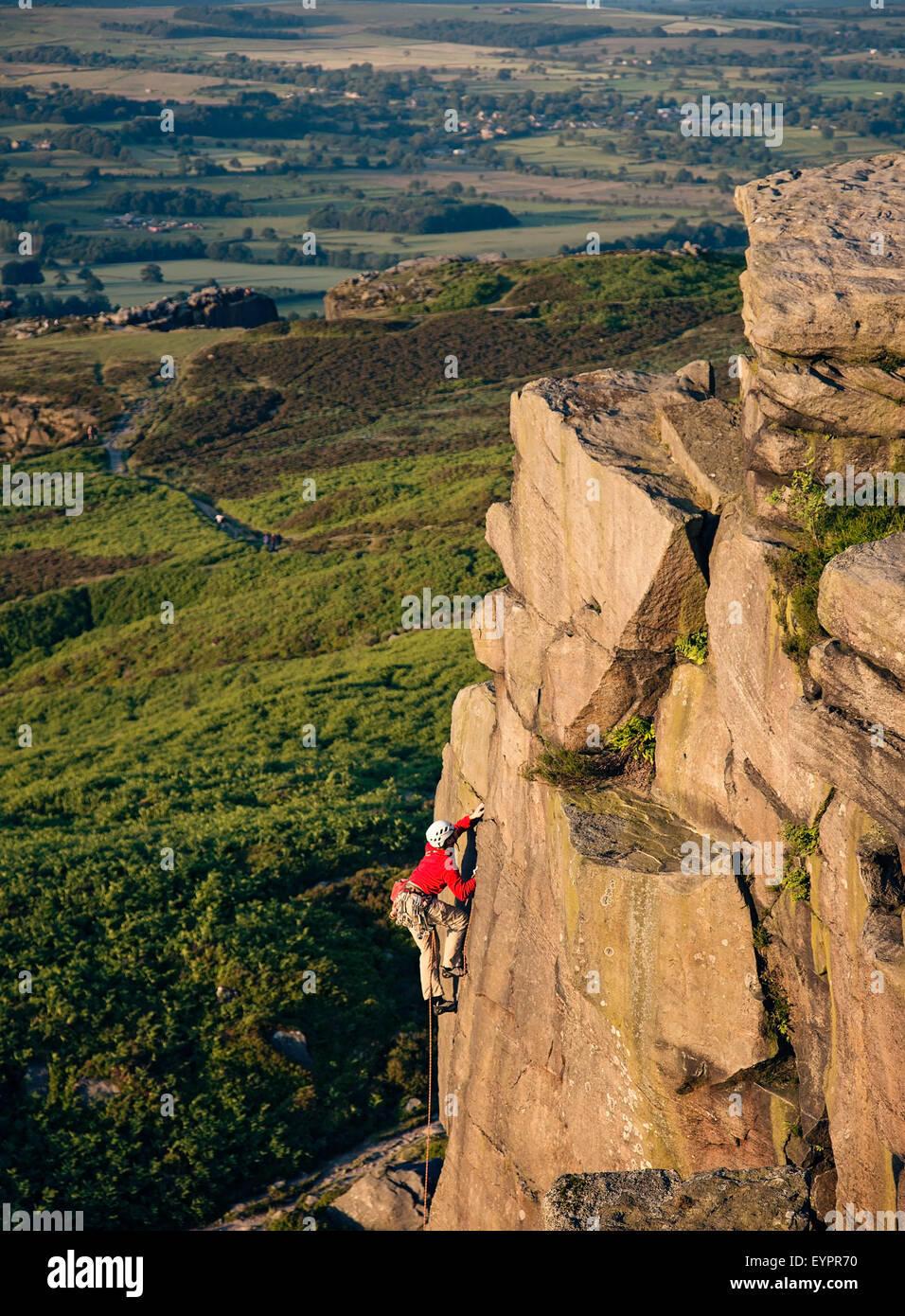 A climber climbing up Ilkley Crags on Ilkley moor Stock Photo