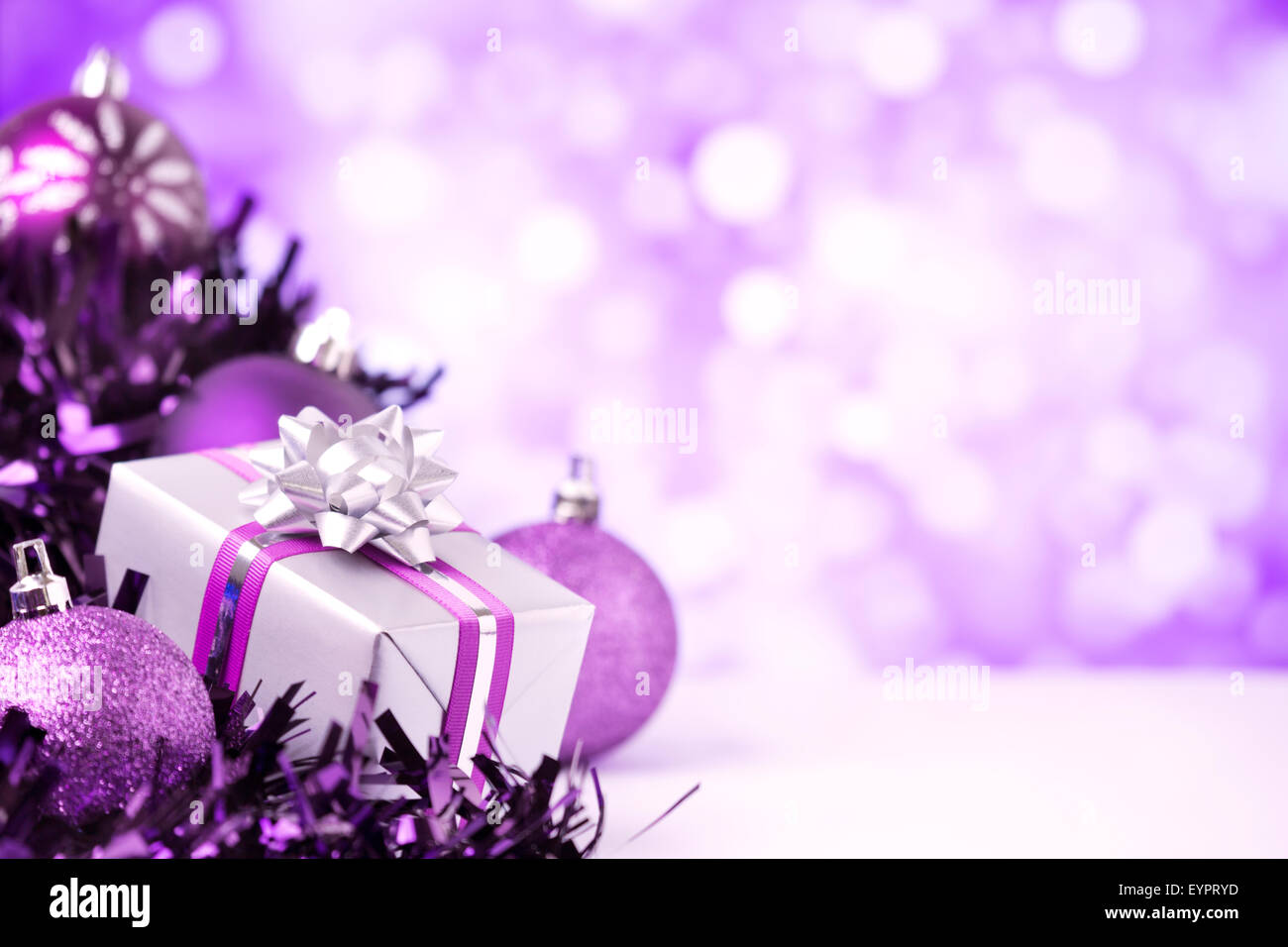 Purple and silver Christmas baubles and a gift in front of defocused purple and white lights. Stock Photo