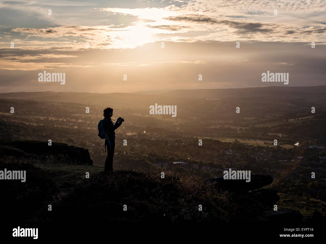 Silhouette of a photographer standing on Ilkley Moor looking over Ilkley at sunset taking photos Stock Photo