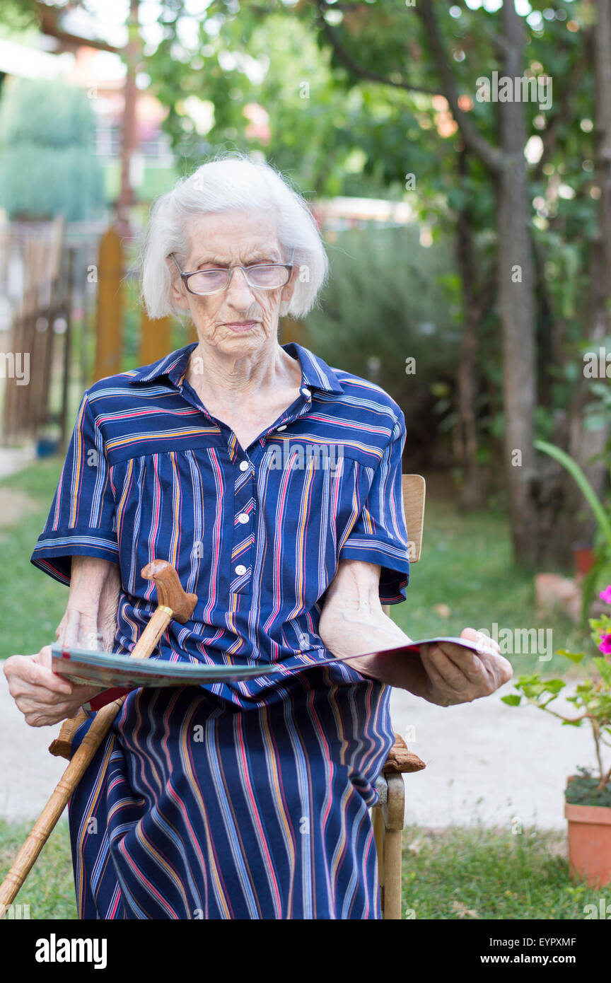 Ninety years old grandma reading the newspapers in the backyard Stock Photo