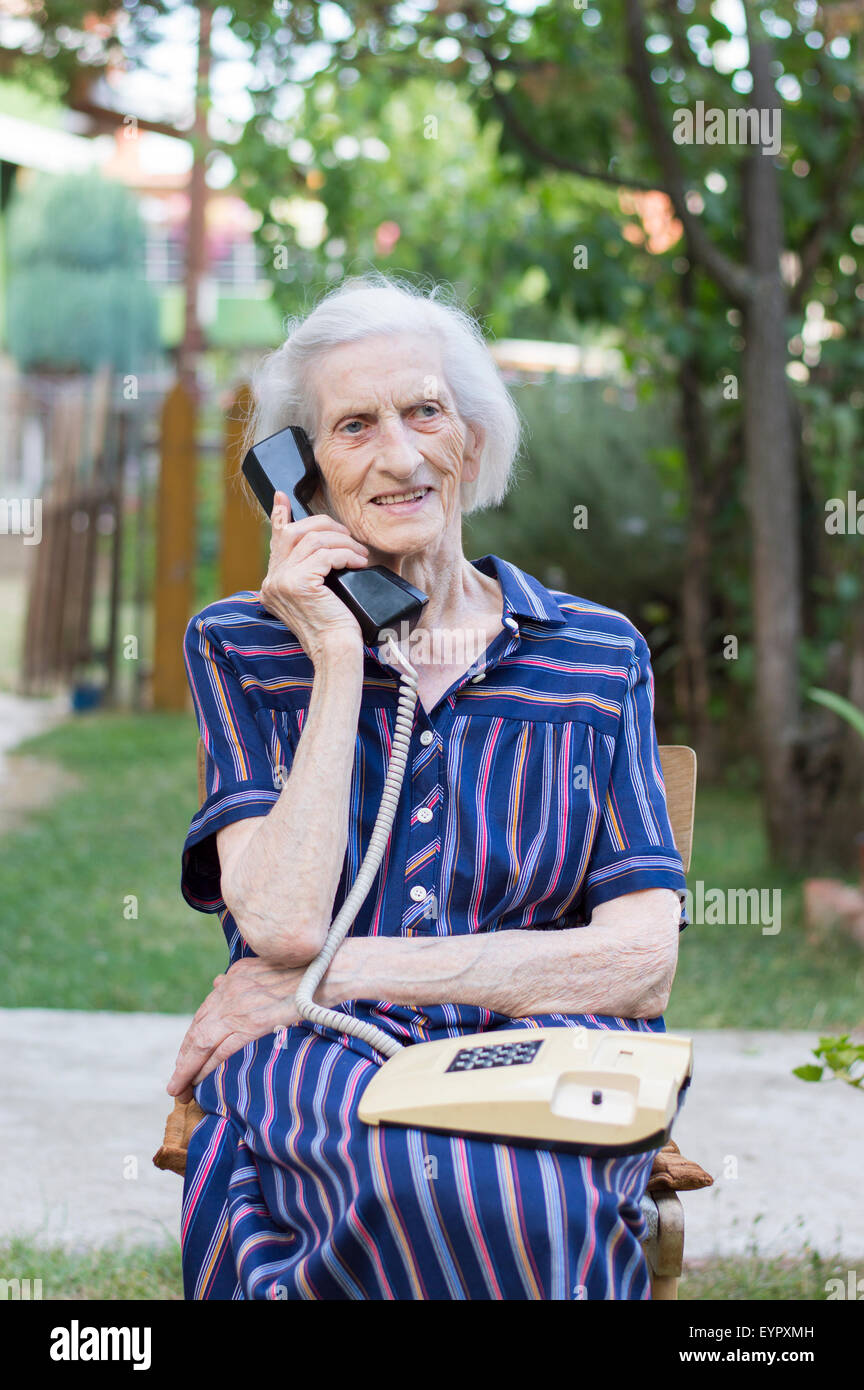 Ninety years old grandma talking on a landline phone in the backyard Stock Photo