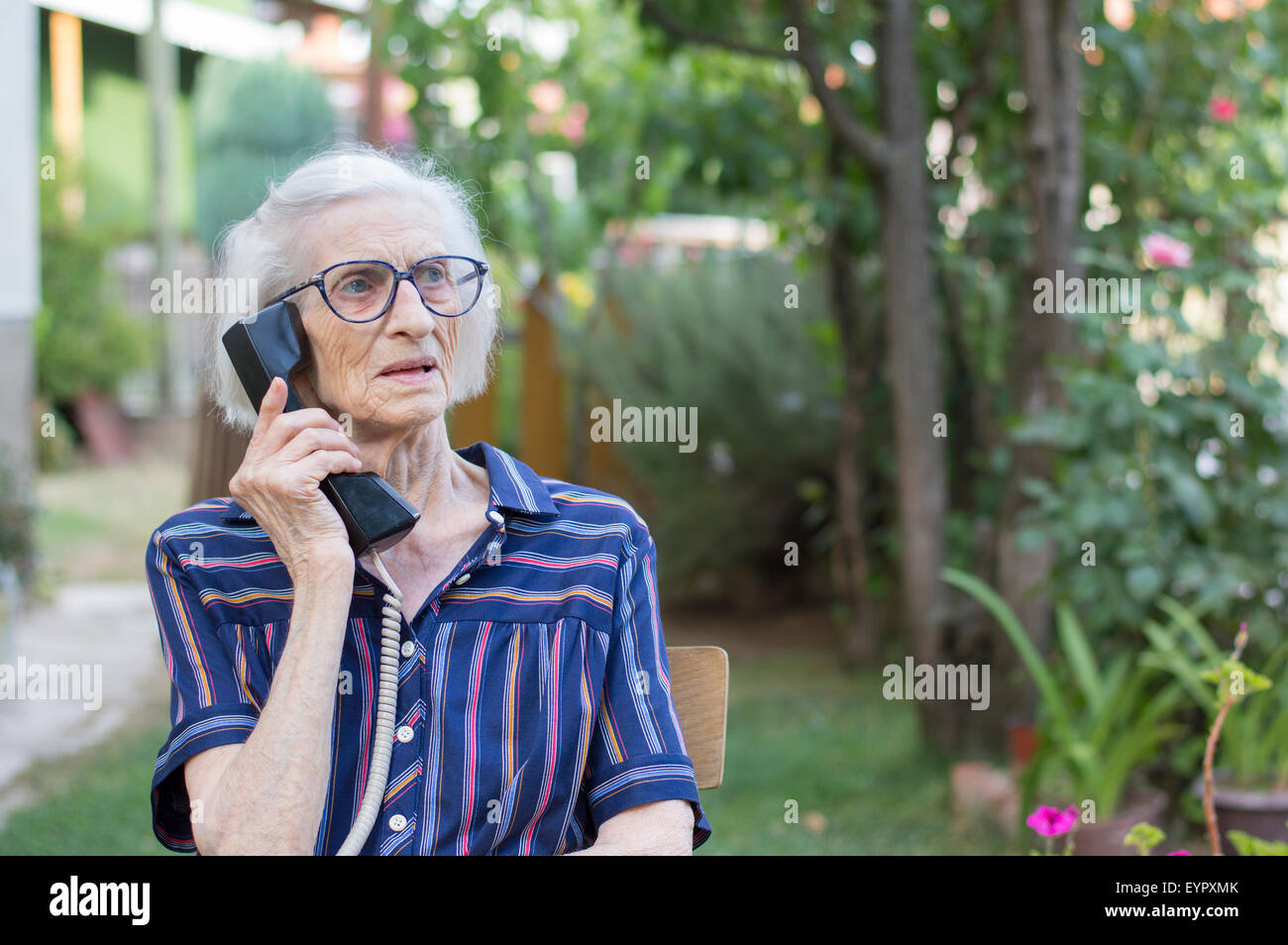 Ninety years old grandma talking on a landline phone in the backyard Stock Photo